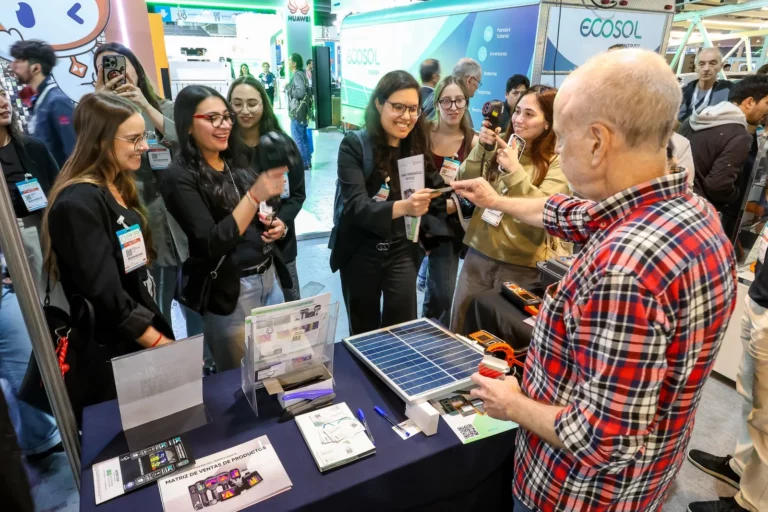 Visitantes escuchan a un expositor junto a un panel solar de demostración